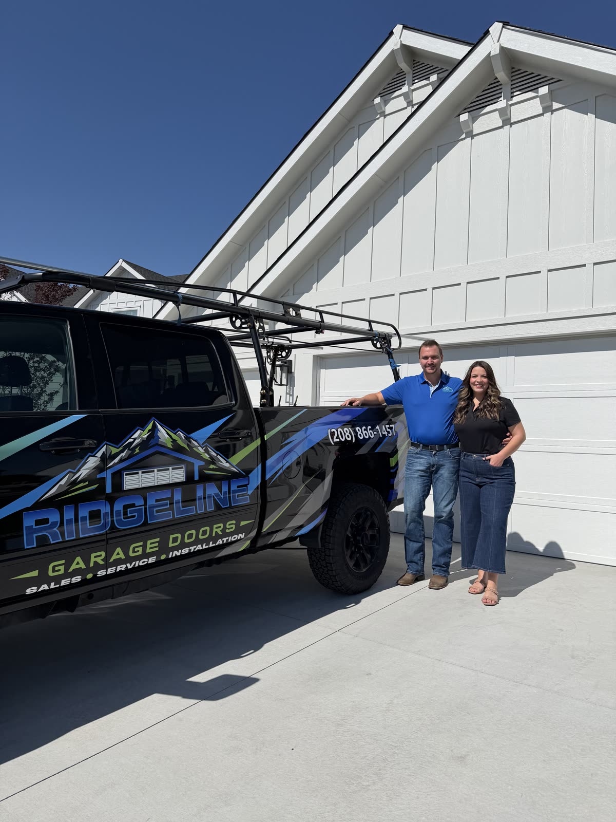 Austin and Kaitlyn, husband-and-wife owners of Ridgeline Garage Doors, standing beside their branded service truck in front of a white garage door in Boise, Idaho